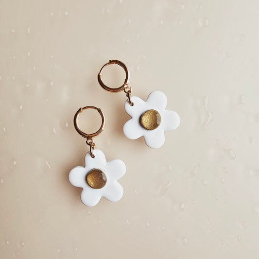 The image shows 2 daisy white earrings. The earrings are a white flower with a gold centre hanging from a gold push back hoop. The daisy flowers are made from polymer clay. 