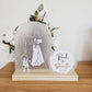 This image shows an illustration on an arch. The illustration is in white vinyl and shows a dog, a groom and a bride in a white wedding dress. The arch is sitting in a pine timber base. There is a circle acrylic shape next to it that says "Paul and Samantha" and the date 4.12.2022.