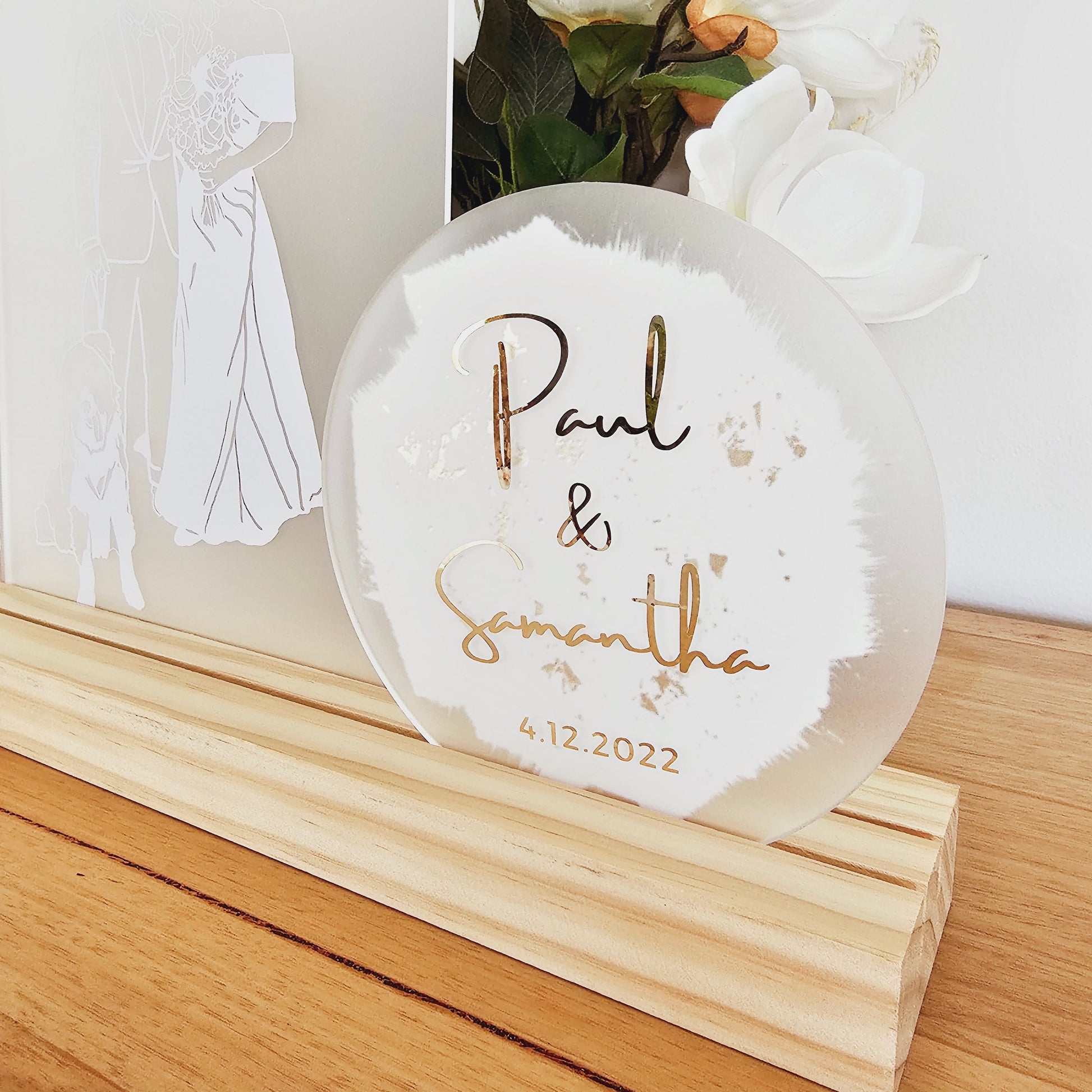 The illustration is in white vinyl and shows a dog, a groom and a bride in a white wedding dress. The arch is sitting in a pine timber base. There is a circle acrylic shape next to it that says "Paul and Samantha" and the date 4.12.2022.